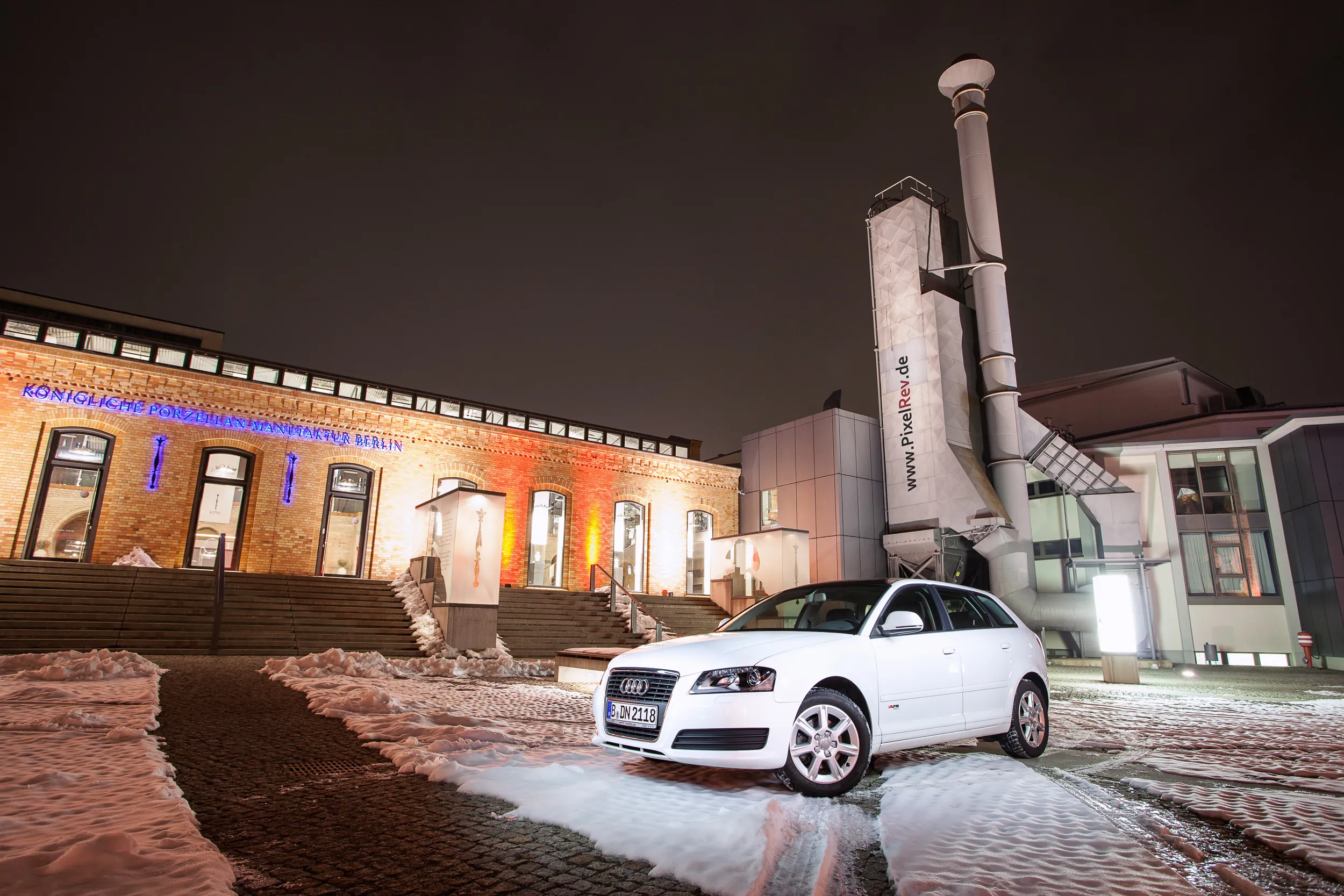 Weißer Audi A3 Sportback nachts im Schnee vor einem beleuchteten Backsteingebäude in Berlin