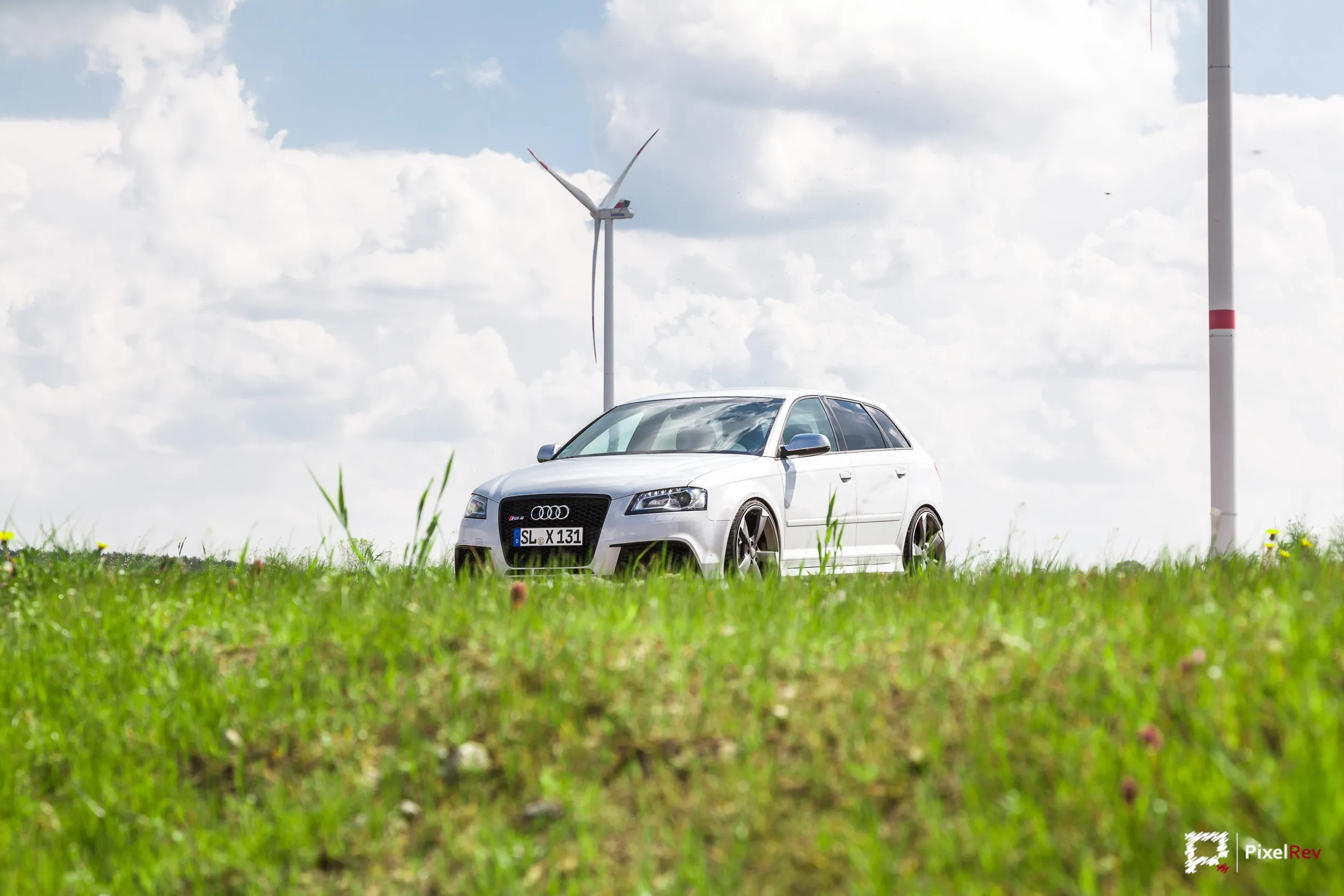 Weißer Audi RS3 Sportback hinter einer Wiese vor Windrädern