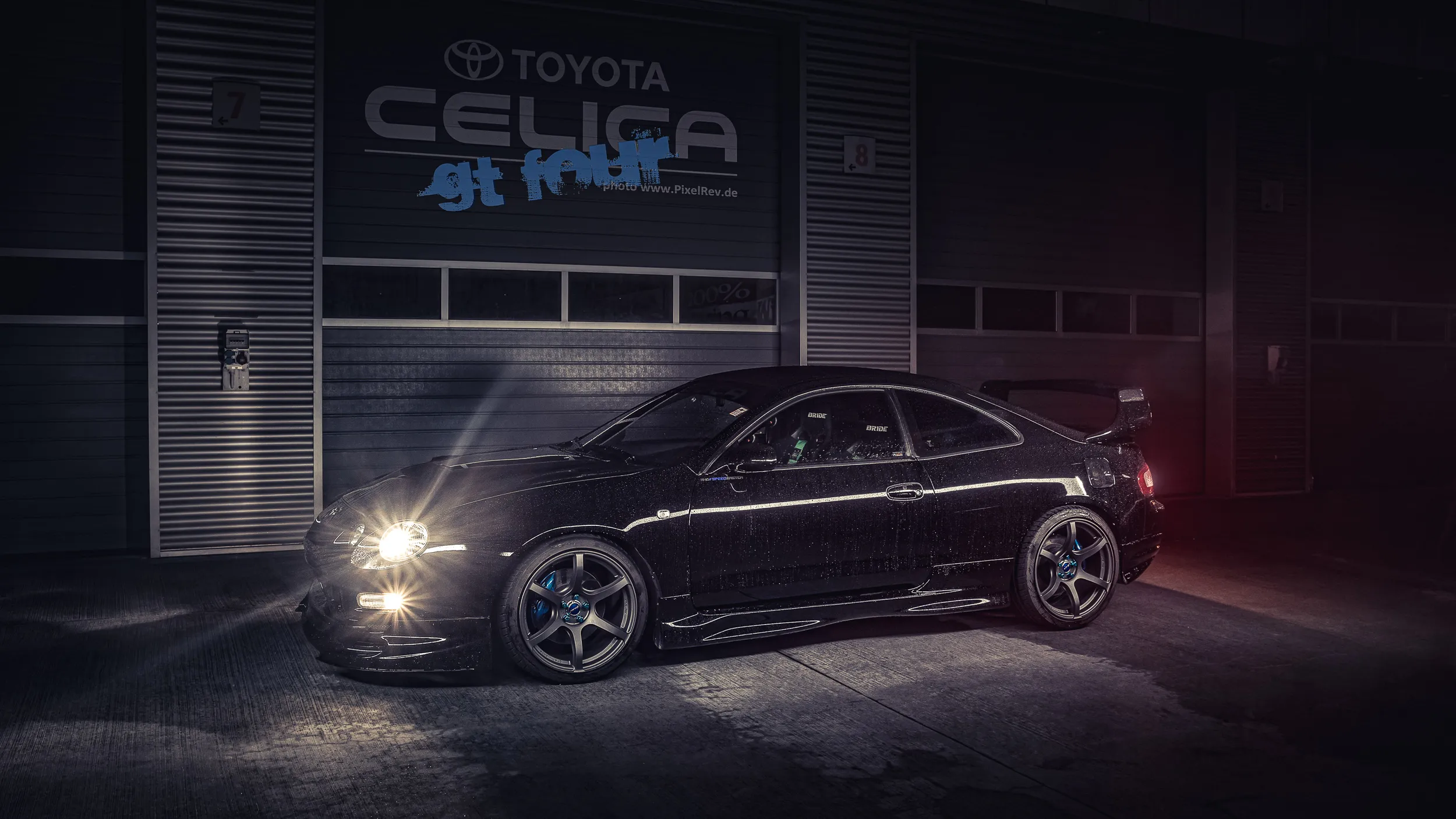 Schwarzes Coupé mit Scheinwerferlicht vor einer Box mit Toyota-Celica-Schriftzug
