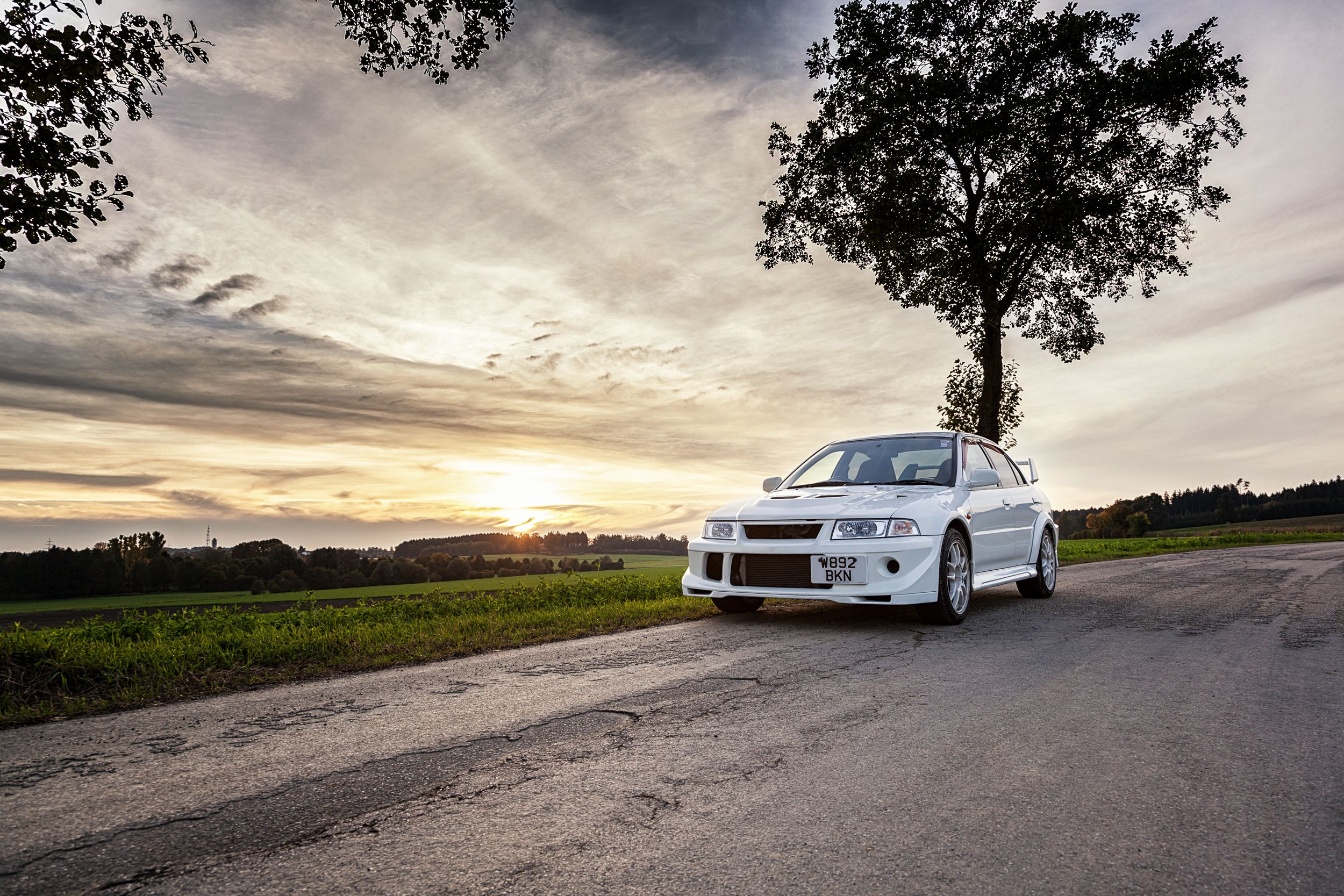 Weißer Mitsubishi Lancer Evolution VI auf einer Landstraße bei Sonnenuntergang