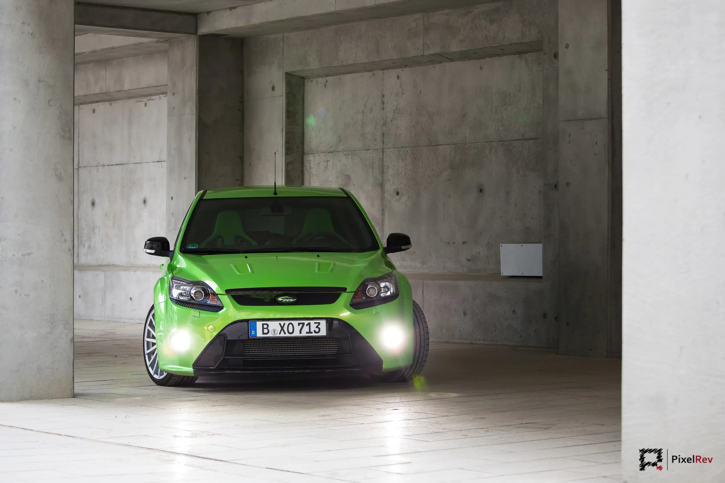 Grüner Ford Focus RS frontal mit eingeschaltetem Licht in einer Betonhalle
