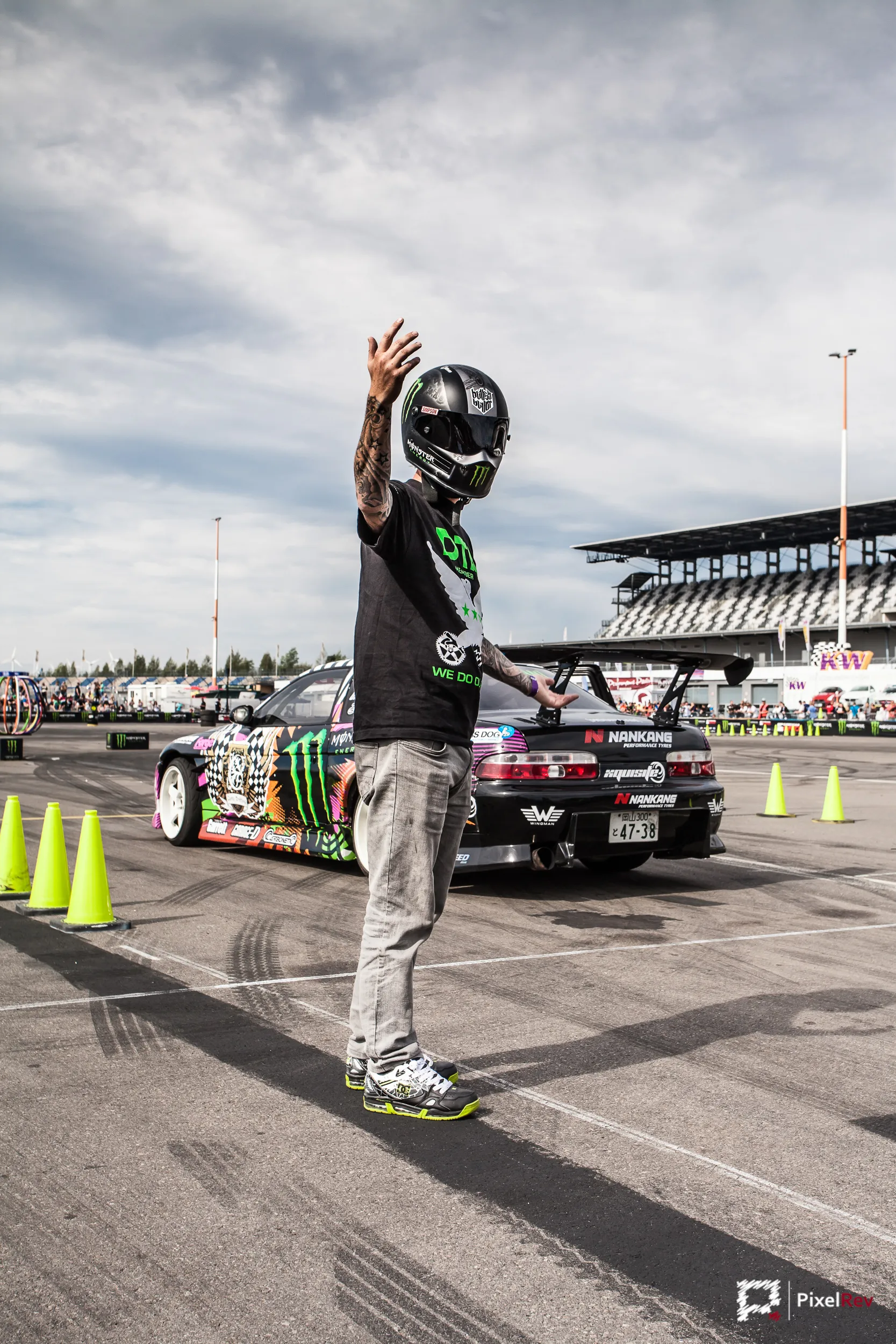 Fahrer mit Helm winkt vor einem Driftfahrzeug beim Gymkhana am Lausitzring