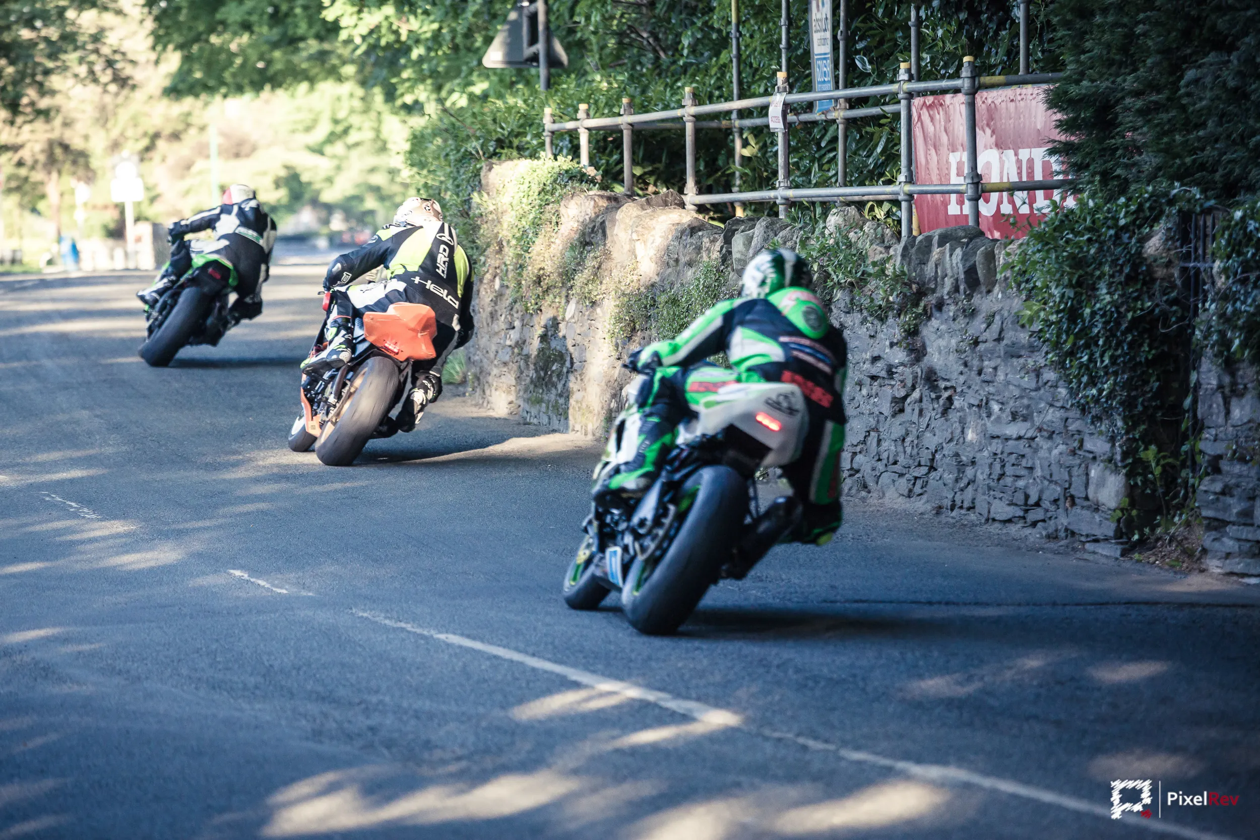 Drei Motorräder in einer Kurve an einer Steinmauer bei der Isle of Man TT