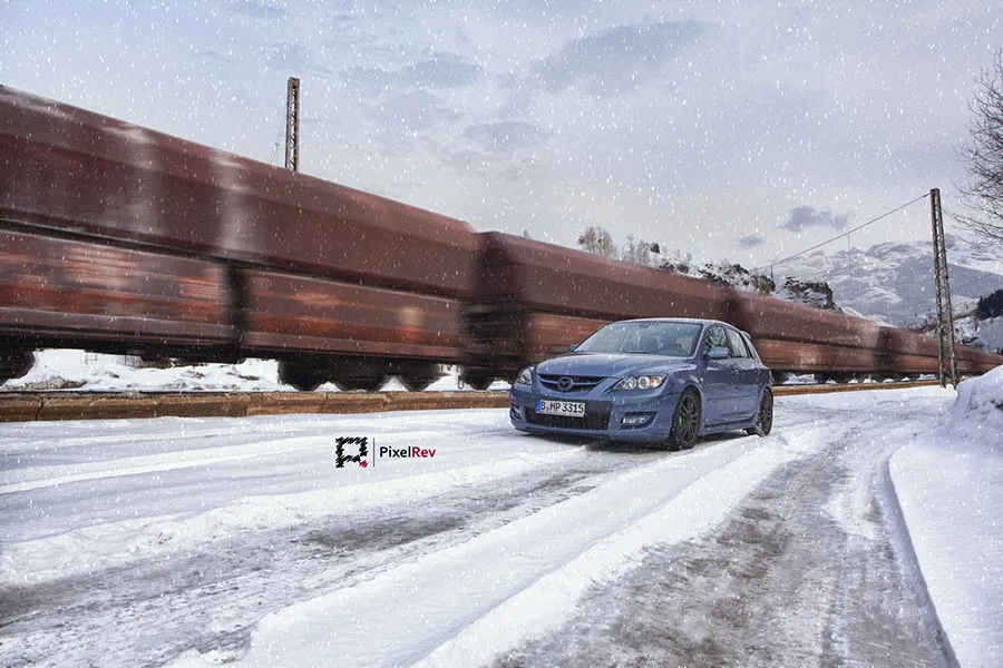 Blauer Mazda 3 MPS im Schnee vor einem vorbeifahrenden Güterzug