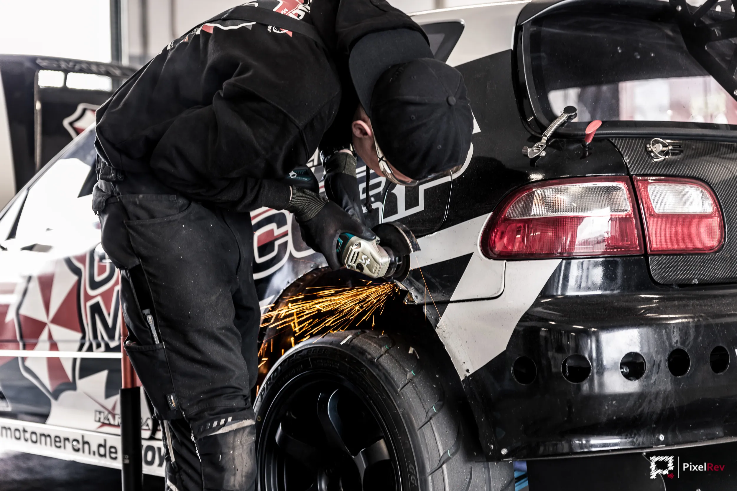 Mechaniker arbeitet mit dem Winkelschleifer an einem Driftfahrzeug, Funken sprühen
