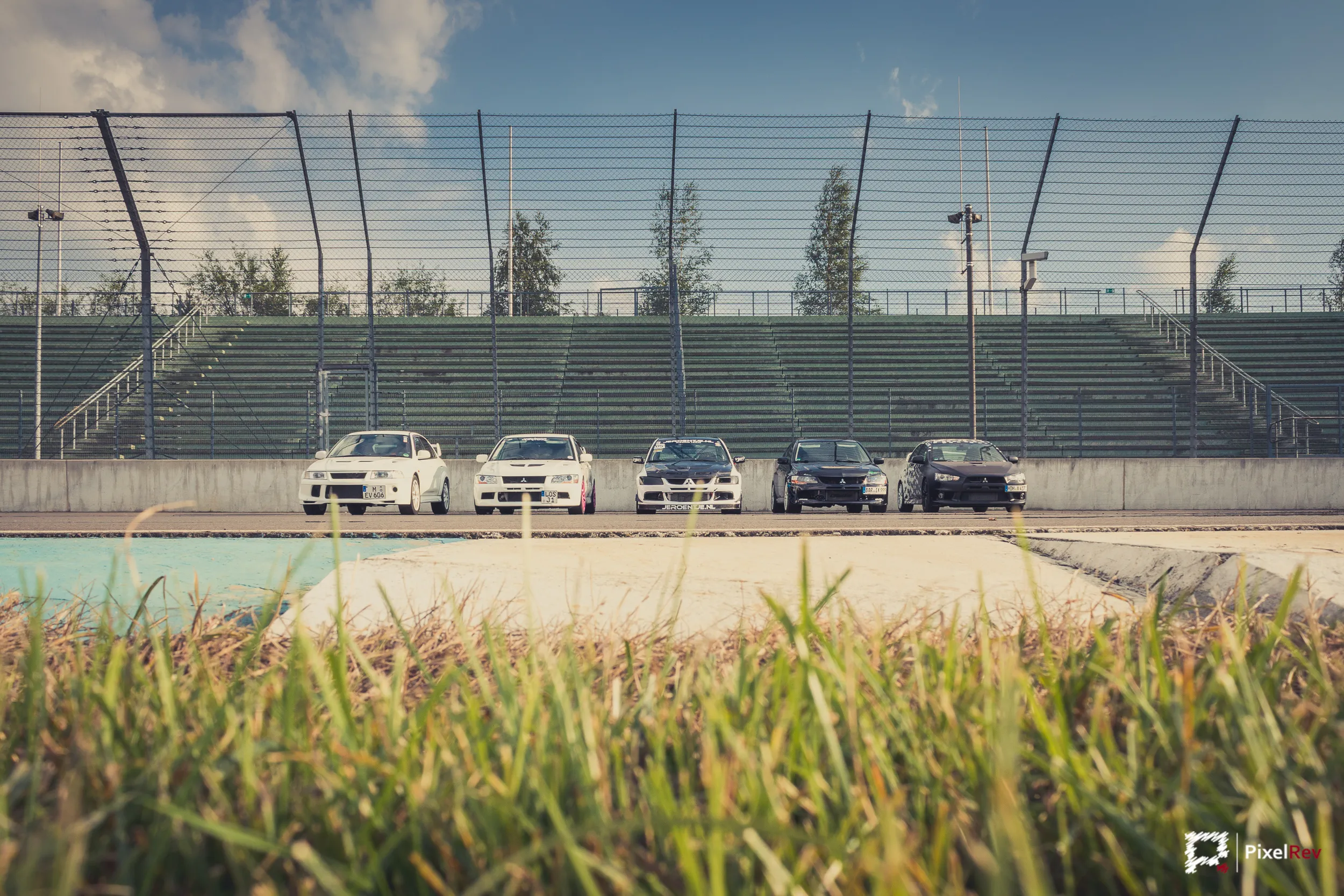 Mitsubishi Lancer Evolution in einer Reihe vor der Tribüne, Gras im Vordergrund