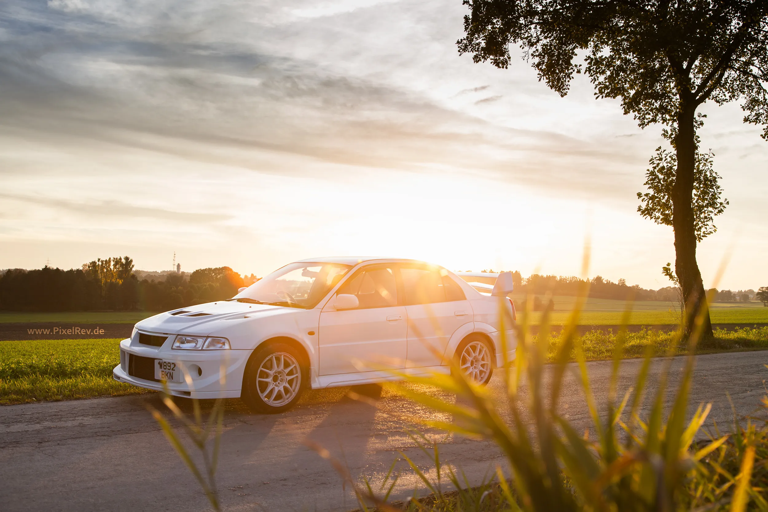 Weißer Mitsubishi Lancer Evolution VI im Gegenlicht auf einer Landstraße bei München