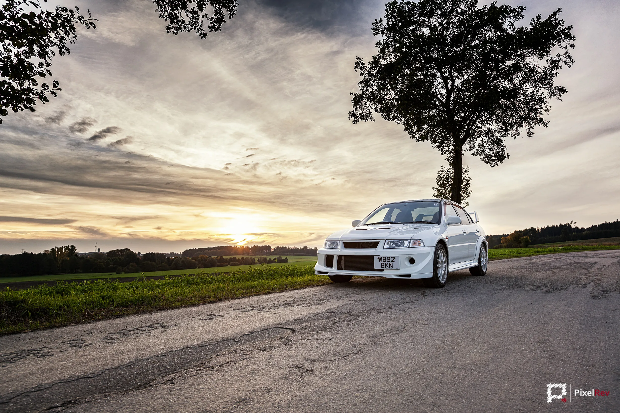 Weißer Mitsubishi Lancer Evolution VI frontal auf einer Landstraße im Sonnenuntergang