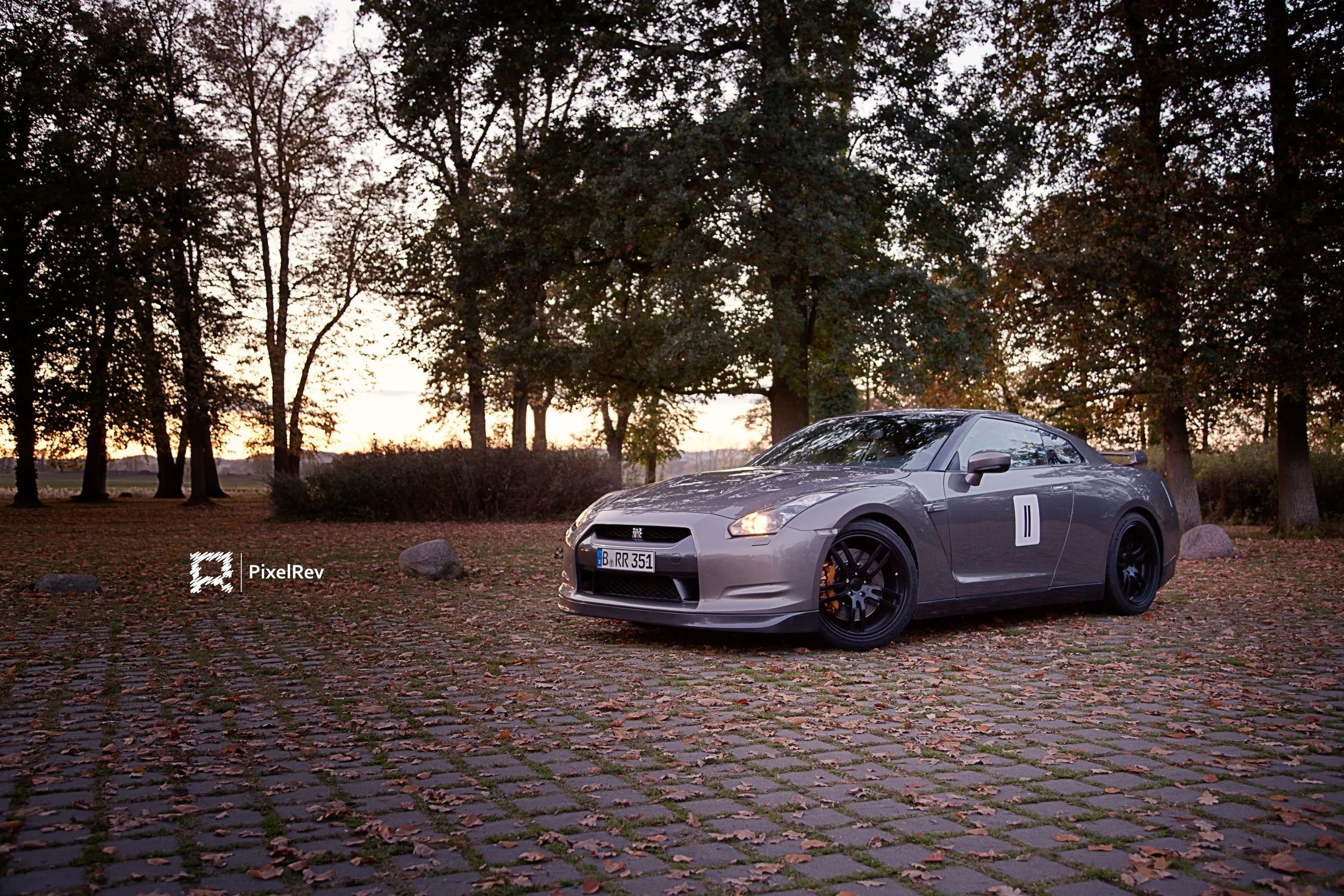 Grauer Nissan GT-R auf Kopfsteinpflaster mit Herbstlaub im Abendlicht
