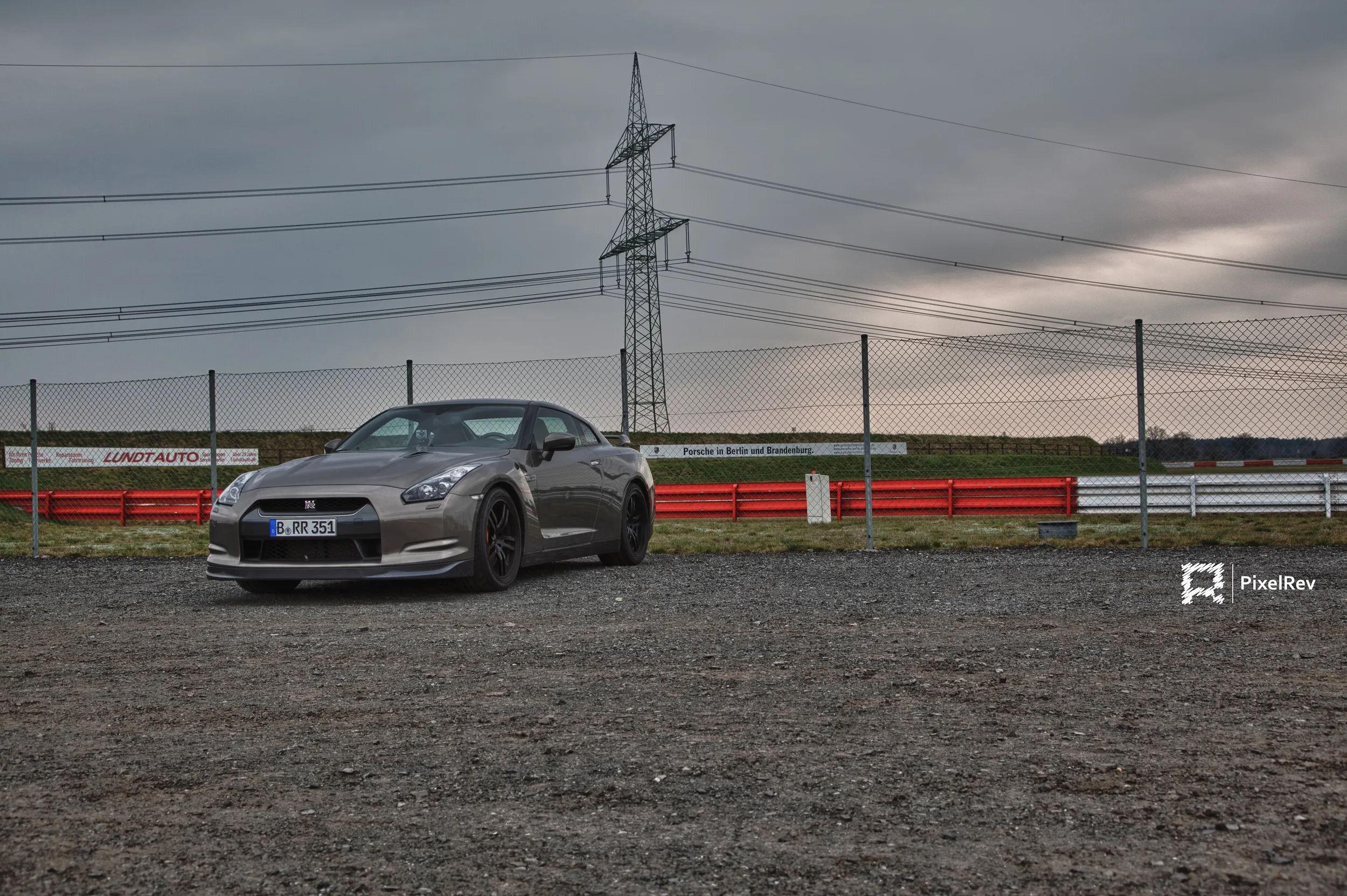 Grauer Nissan GT-R R35 auf Schotter vor einem Strommast