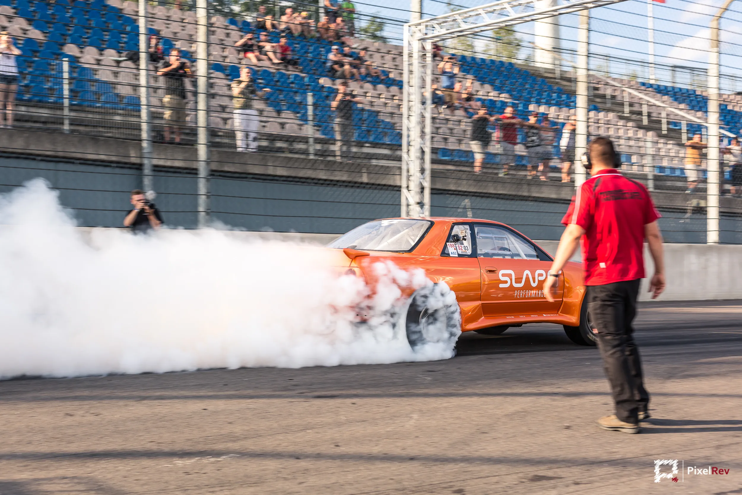 Orangefarbener Nissan Skyline R32 beim Burnout vor der Tribüne