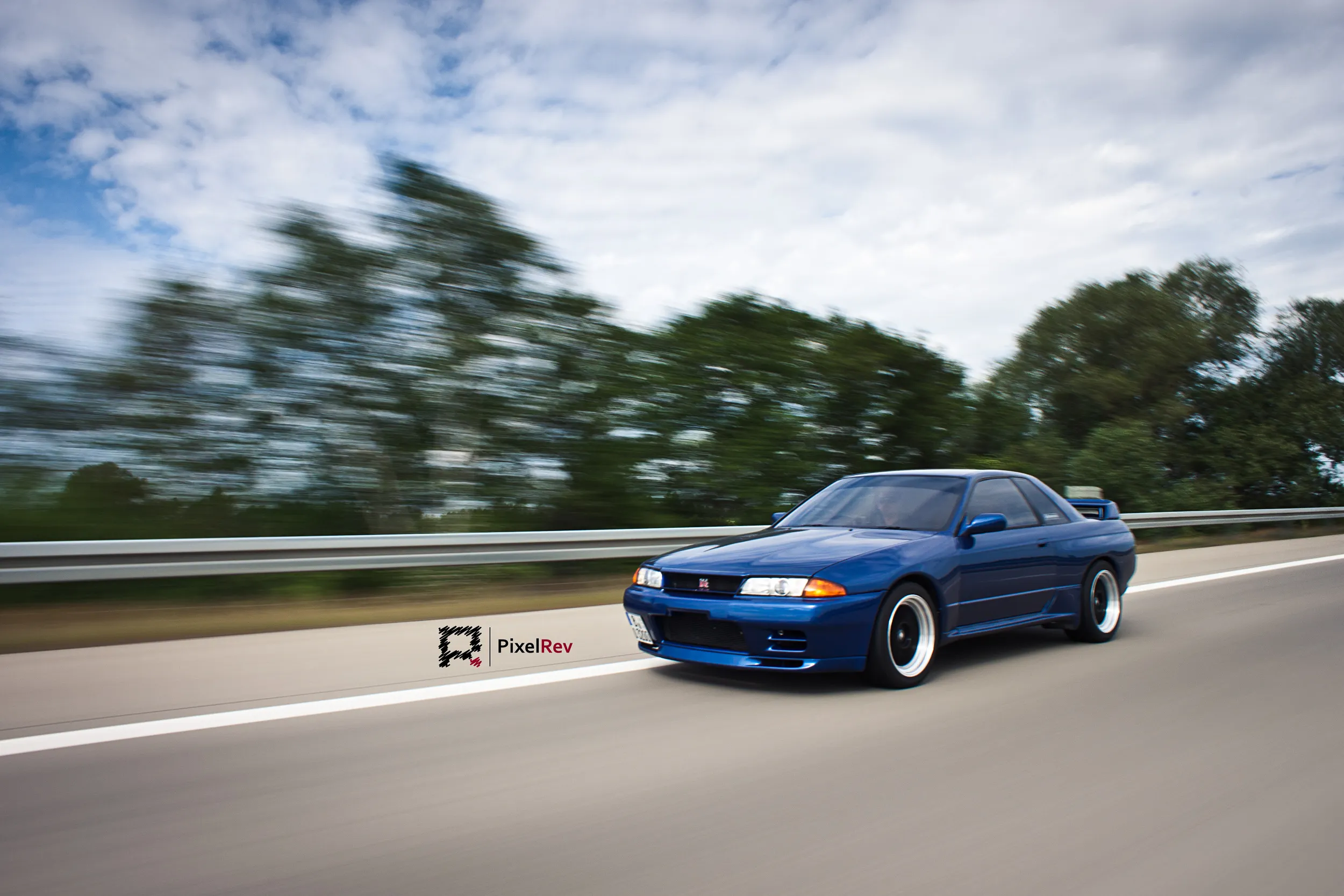 Blauer Nissan Skyline R32 GT-R in Fahrt auf der Autobahn, Bäume in Bewegungsunschärfe