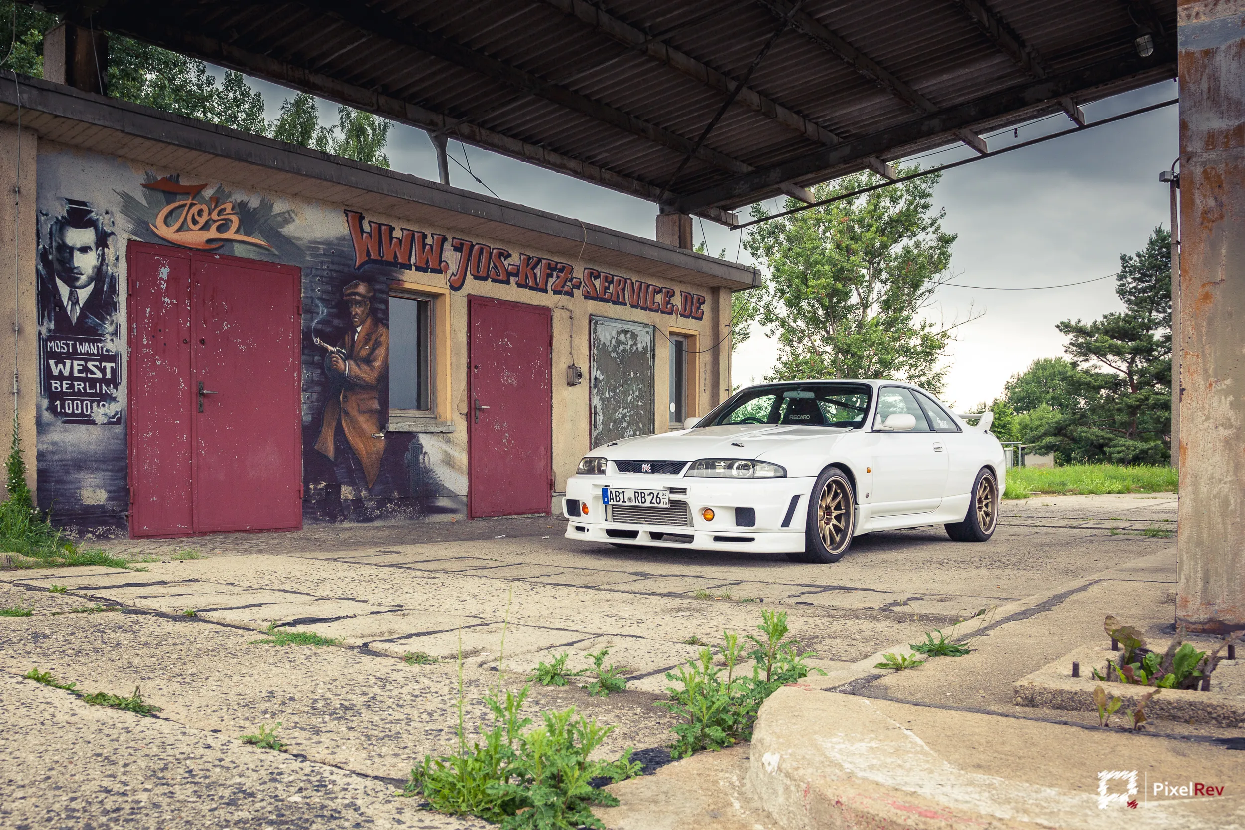 Weißer Nissan Skyline R33 GT-R vor einer Werkstatt mit Graffiti