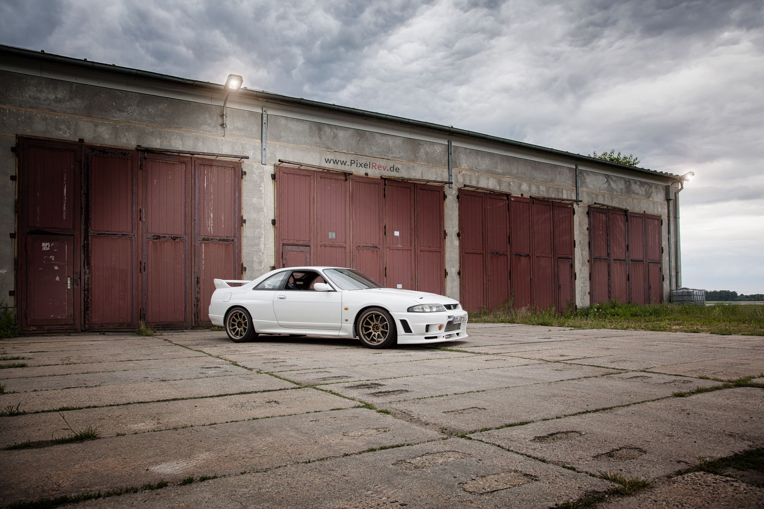 Weißer Nissan Skyline R33 GT-R vor einem alten Hangar