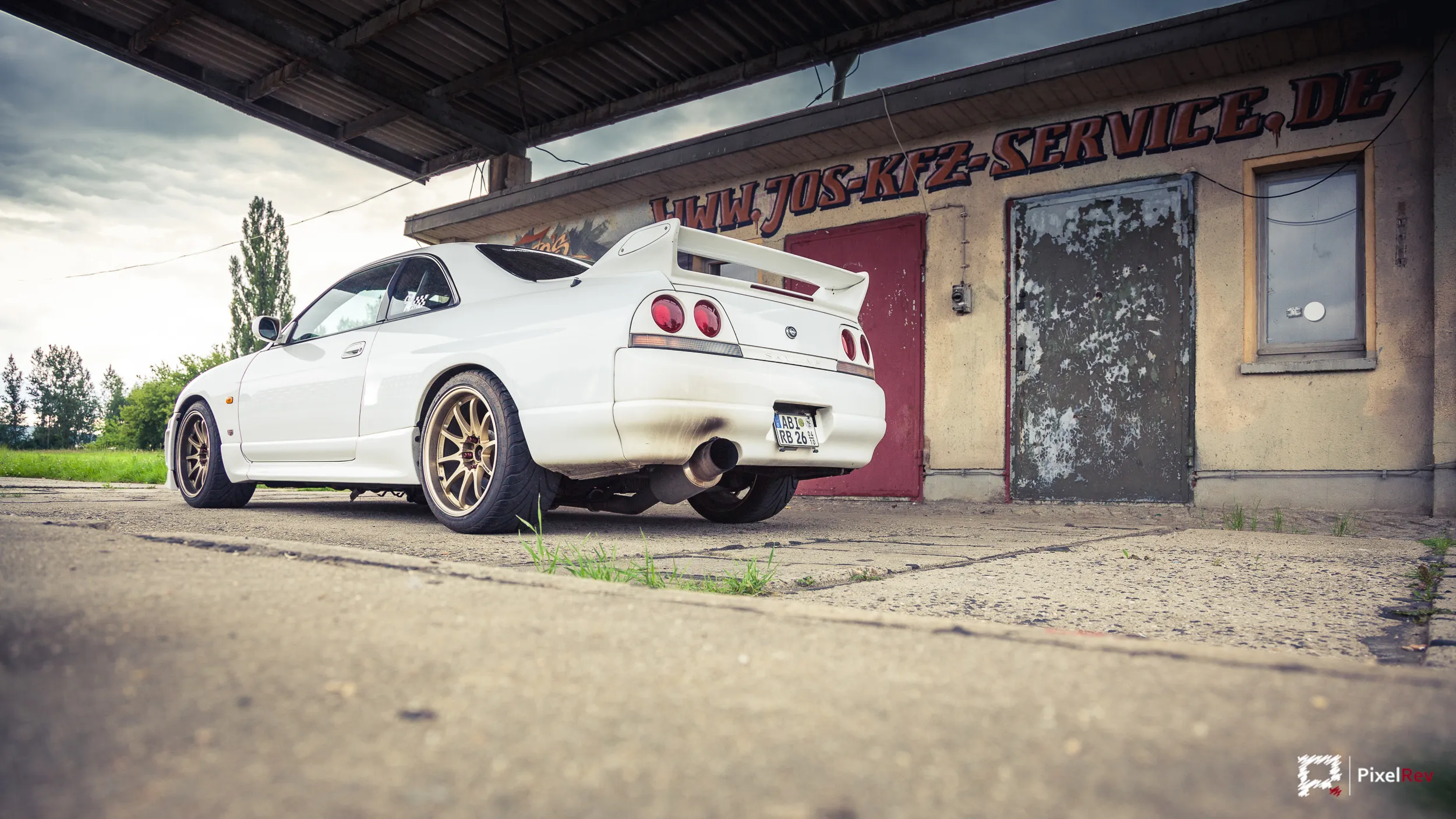Heck des weißen Nissan Skyline R33 GT-R vor einer Werkstatt mit Graffiti