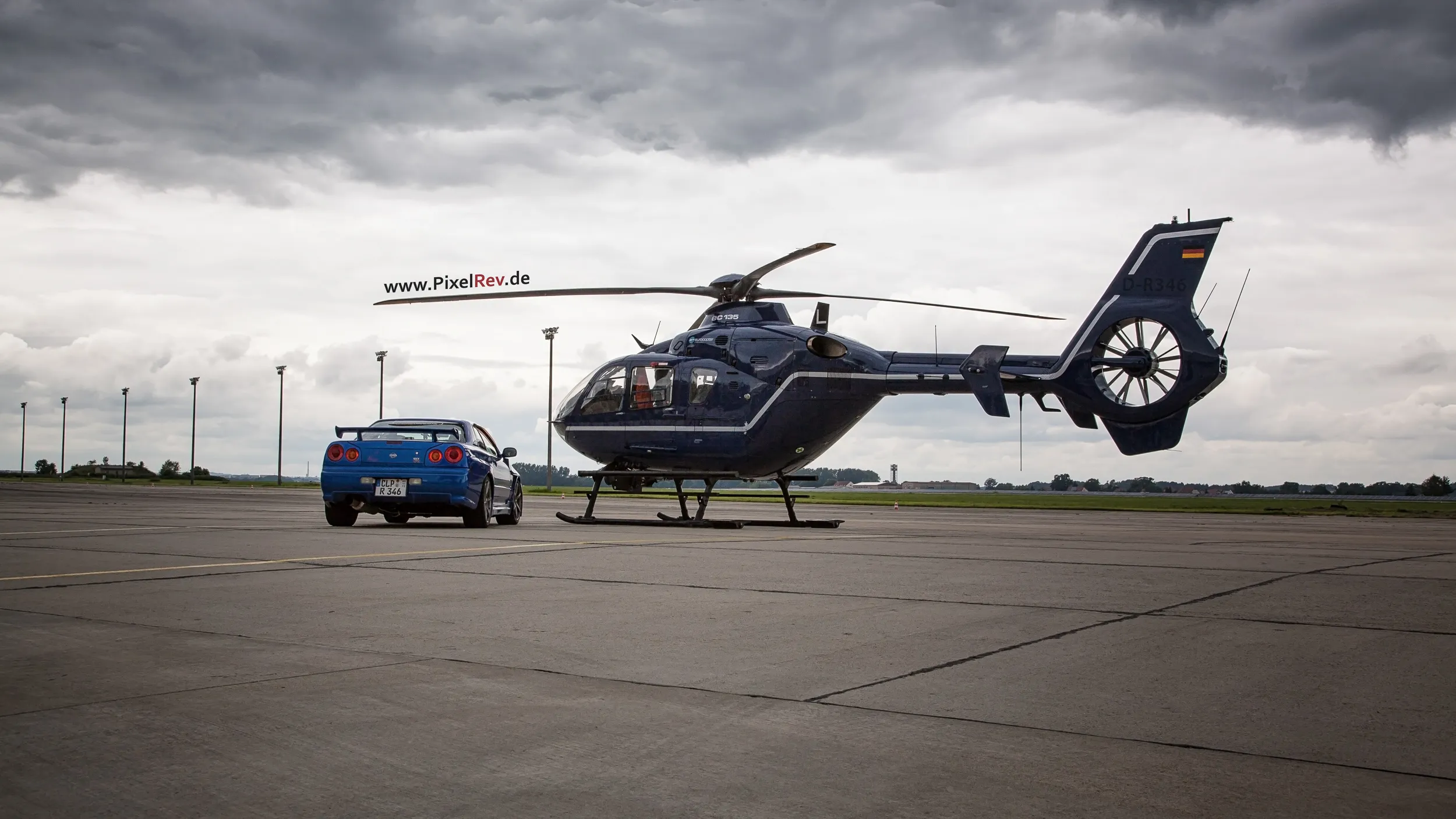 Blauer Nissan Skyline R34 GT-R neben einem Hubschrauber auf dem Rollfeld