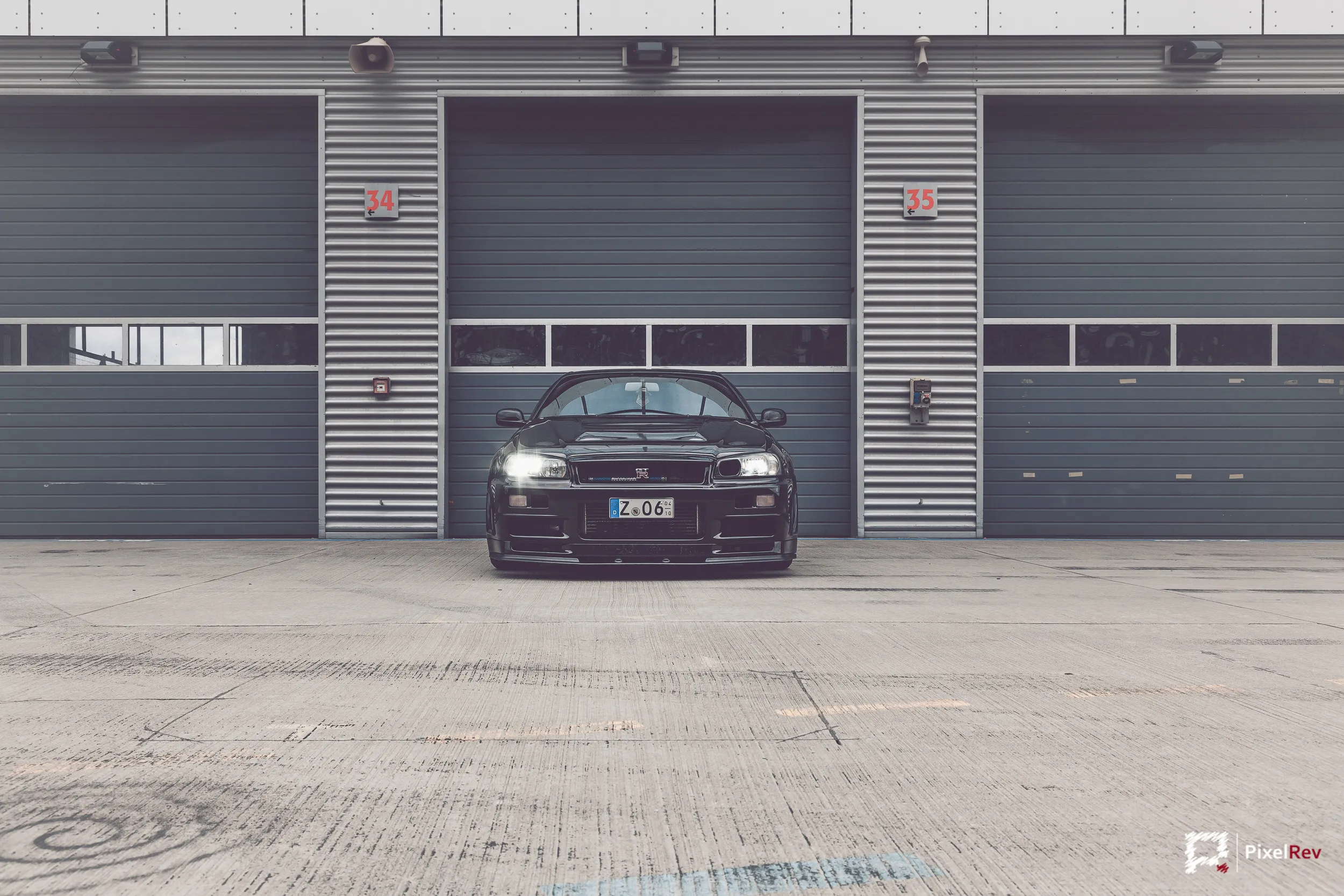 Nissan Skyline R34 GT-R Nismo Omori S1 frontal vor einem geschlossenen Rolltor