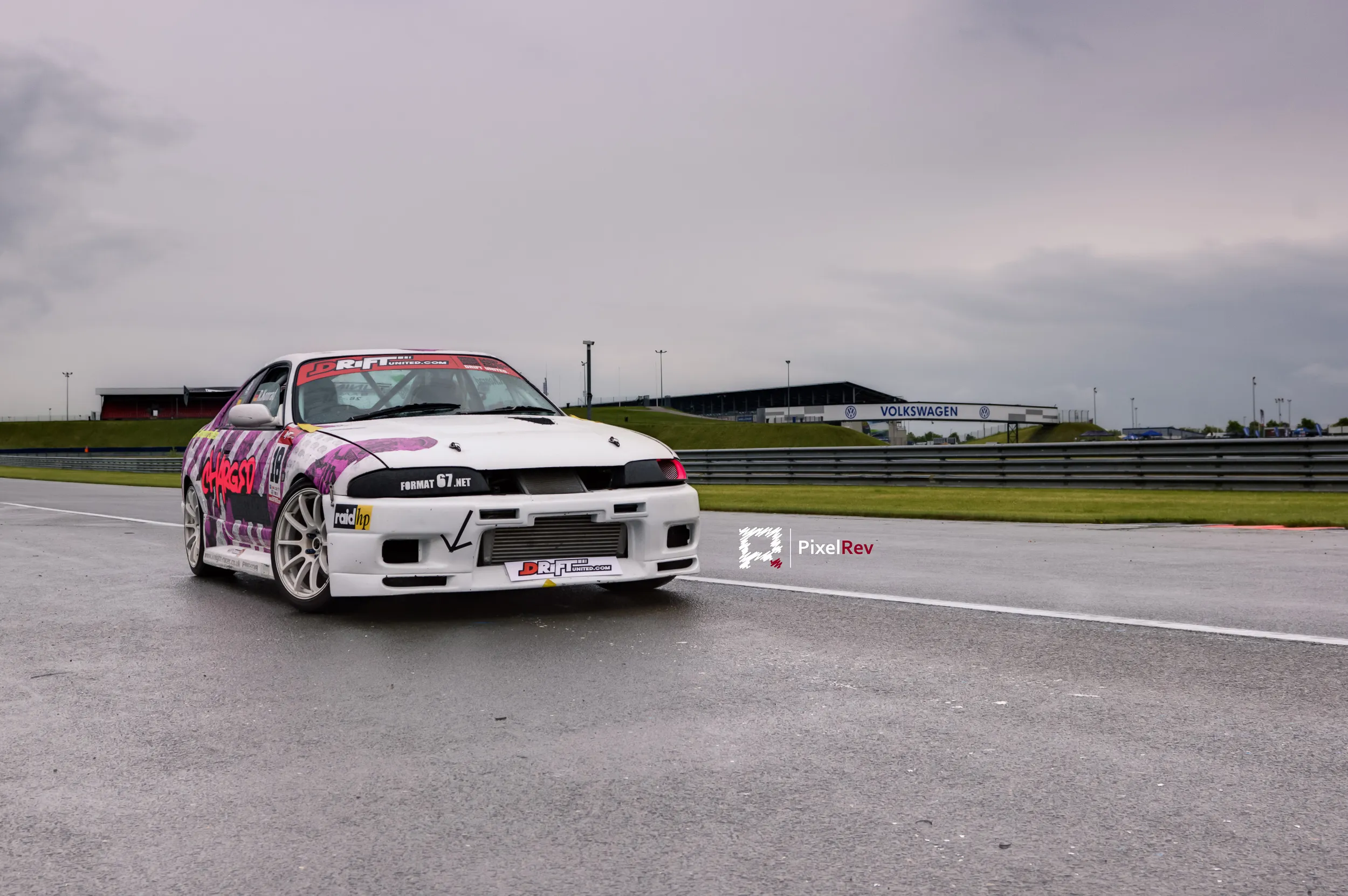 Nissan Skyline R33 in bunter Drift-Folierung auf nasser Rennstrecke