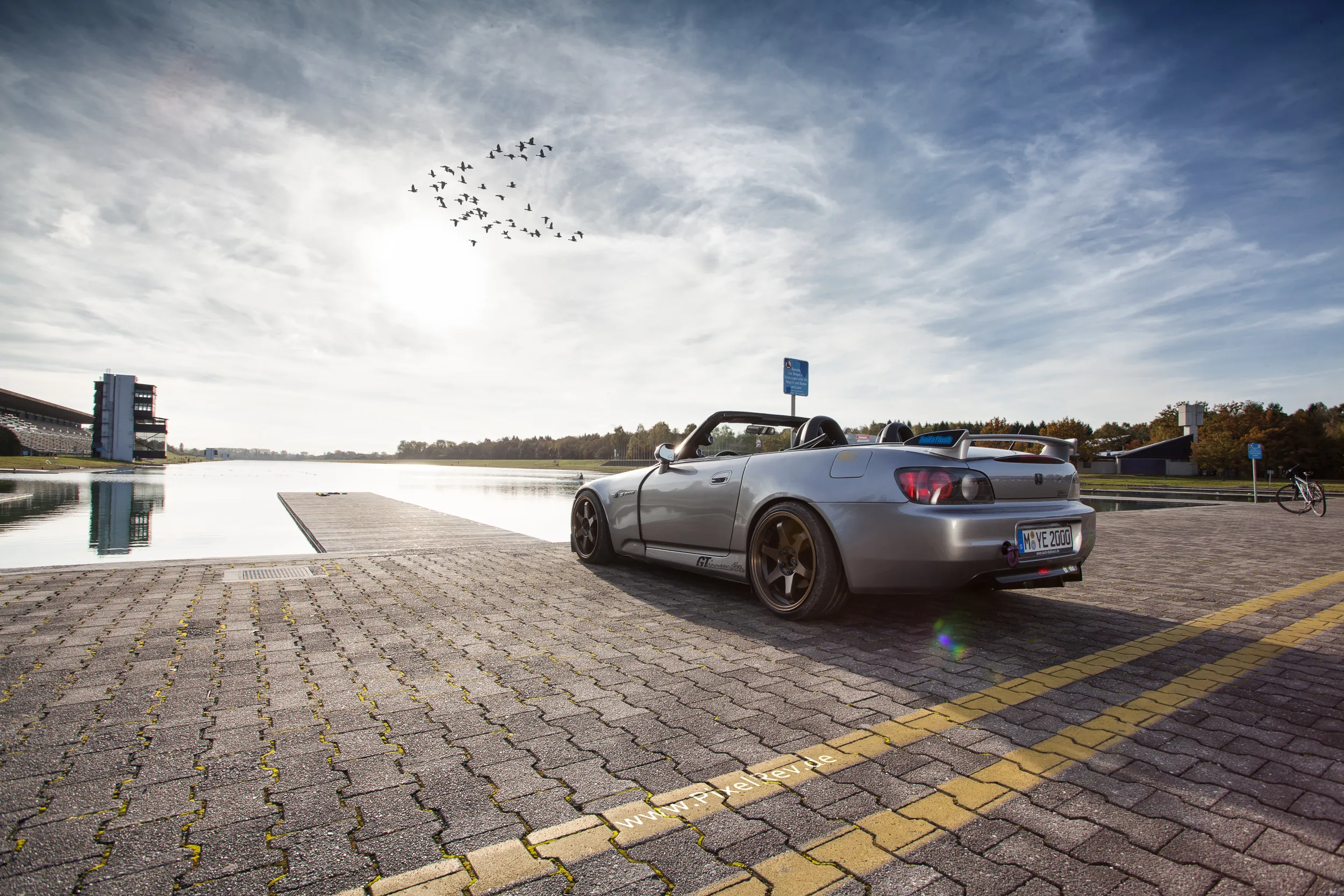 Silberner Honda S2000 Roadster mit offenem Verdeck an einer Regattastrecke im Gegenlicht