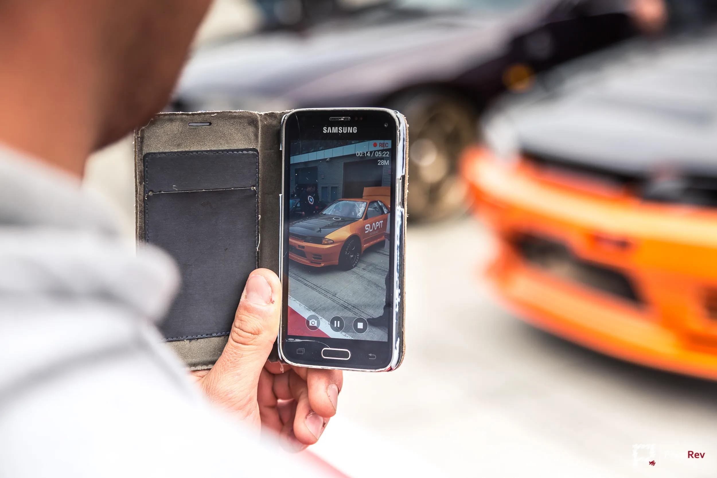 Besucher filmt mit dem Smartphone ein orangefarbenes Driftfahrzeug