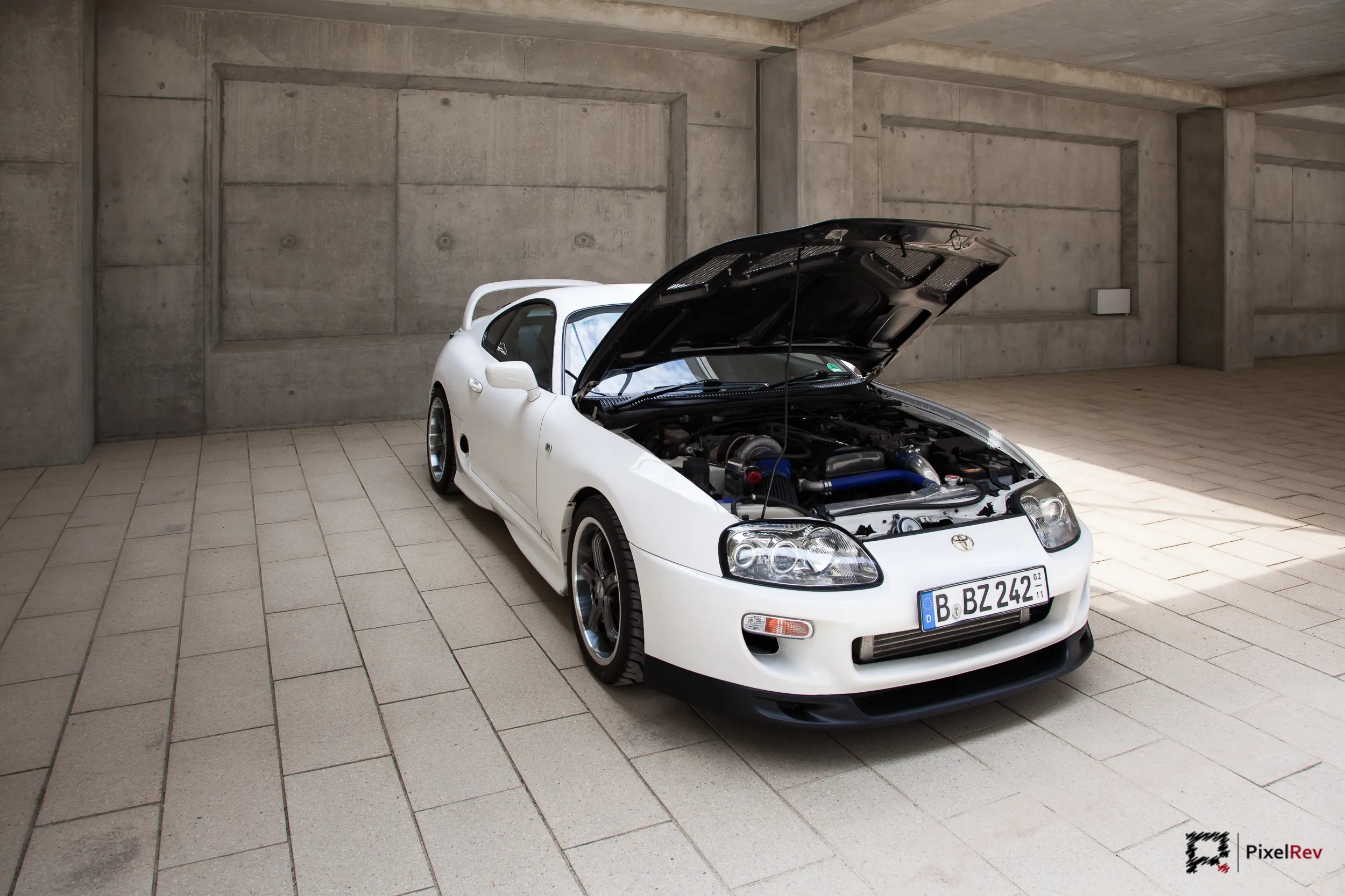 Weißer Toyota Supra mit geöffneter Motorhaube in einer Halle