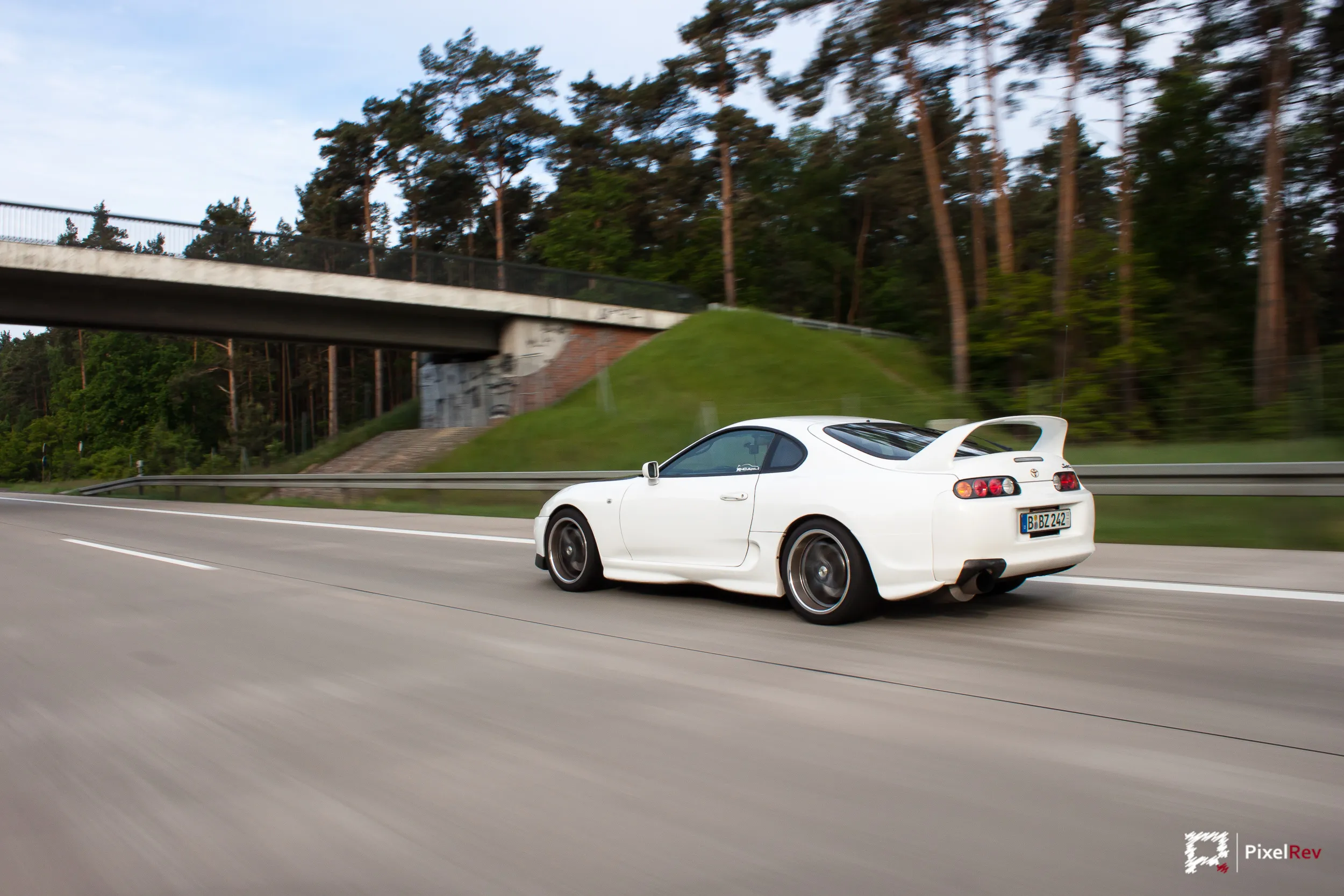 Weißer Toyota Supra in Fahrt auf der Autobahn vor einer Brücke