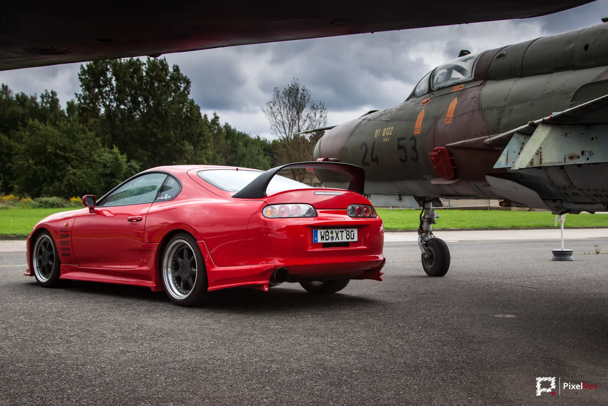 Roter Toyota Supra mit Heckflügel neben einem Kampfjet in Berlin-Gatow