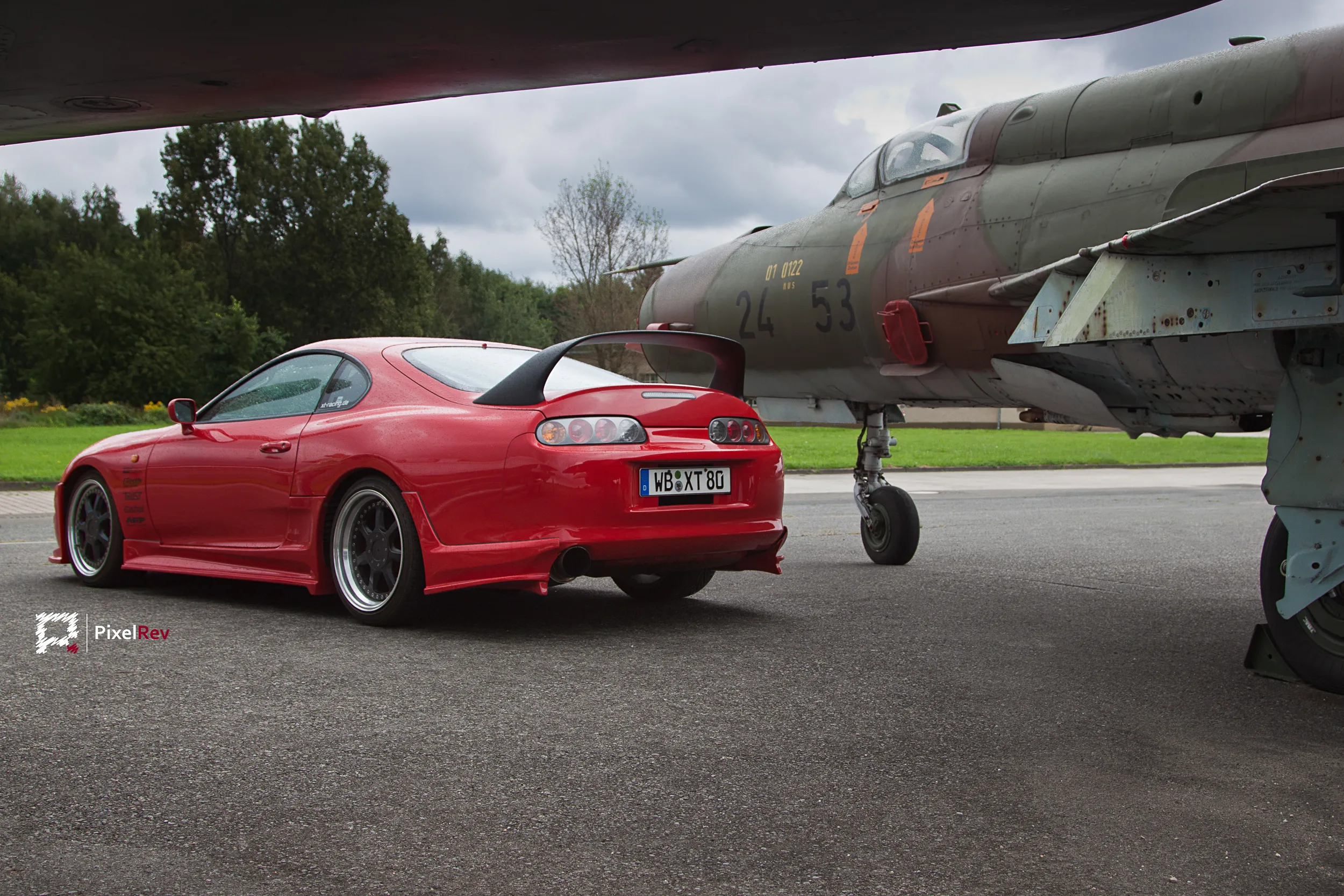 Roter Toyota Supra mit Heckflügel neben einem Kampfjet in Berlin-Gatow