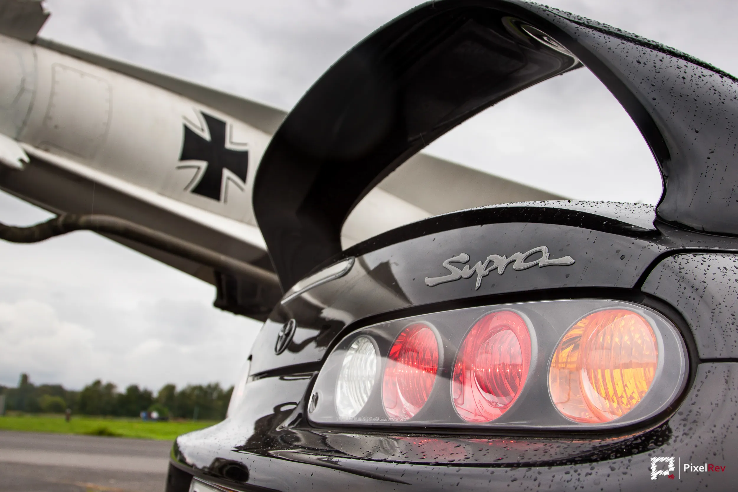 Rückleuchten und Supra-Schriftzug eines schwarzen Toyota Supra vor einem Flugzeugleitwerk