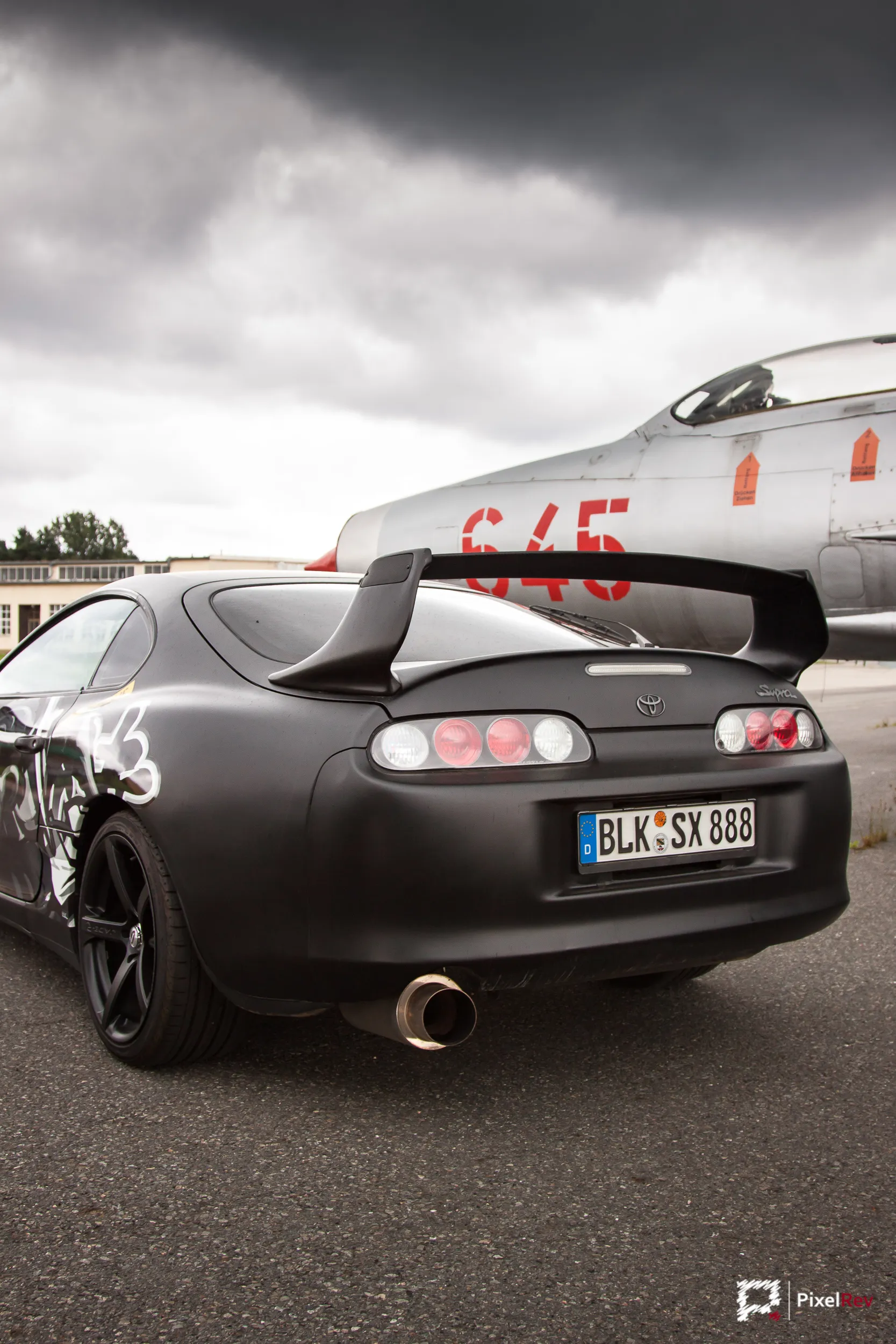 Heck des schwarzen Toyota Supra vor einem MiG-21-Kampfjet